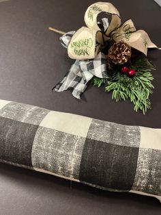 a plaid pillow sitting on top of a table next to a pine cone and ribbon