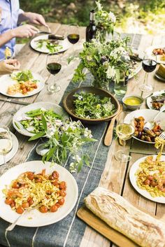 an outdoor table is set with food and wine