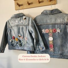 two denim jackets with embroidered flowers on them hanging from a coat rack, one is blue and the other has pink roses