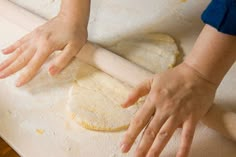 a person rolling out dough on top of a pizza crust with their hands resting on it