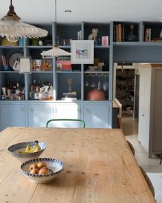 a wooden table topped with two bowls filled with fruit next to a blue bookcase