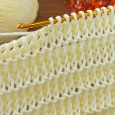 a close up view of a crochet stitch with yarn and knitting needles in the background