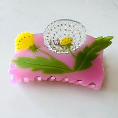 a pink and green object with flowers on it's side sitting on a white surface