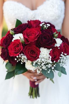 a bridal holding a bouquet of red roses and white baby's breath flowers