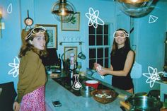 two women standing in a kitchen with glasses on their head and cooking food together,