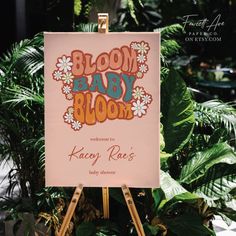 an easel with a sign that says bloom baby bloom on it in front of some plants