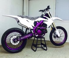 a purple and white dirt bike sitting on top of a stand in front of a window