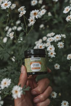 a person holding a jar of honey in front of some daisies and wildflowers