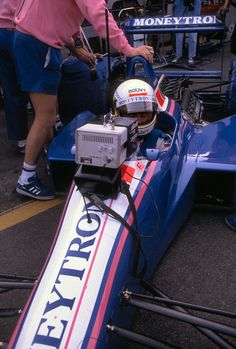 a man sitting in a racing car on top of a race track next to other people