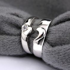 two silver rings sitting on top of a gray pillow next to each other with diamonds in the middle