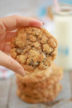 a person holding up a cookie next to a glass of milk