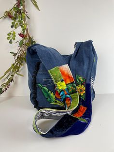 a blue purse with flowers painted on the front and side, sitting next to a plant