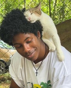 a cat sitting on top of a woman's head in front of a fence