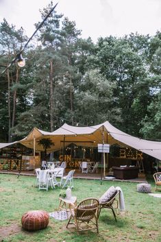 a tent set up in the middle of a field with chairs and tables under it