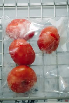 three tomatoes wrapped in plastic sitting on a rack