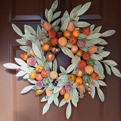 a wreath with leaves and fruit hanging on the front door to welcome people into the house