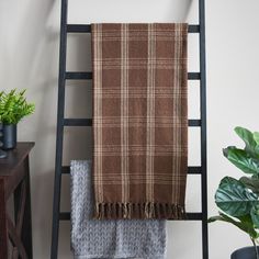 a brown and white plaid blanket sitting on top of a ladder next to a potted plant