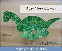 a green paper plate dinosaur sitting on top of a wooden table