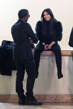 a man and woman sitting on a bench talking to each other in front of a wall