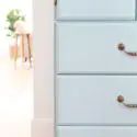 a white dresser with three drawers and two knobs on the front, one drawer has a smiley face drawn on it