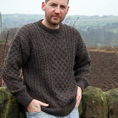 a man standing next to a stone wall with his hands in his pockets and looking at the camera