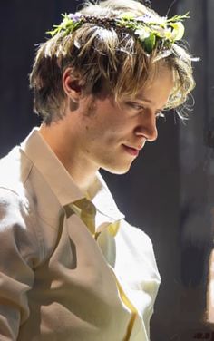 a young man with a flower crown on his head looking down at something in front of him