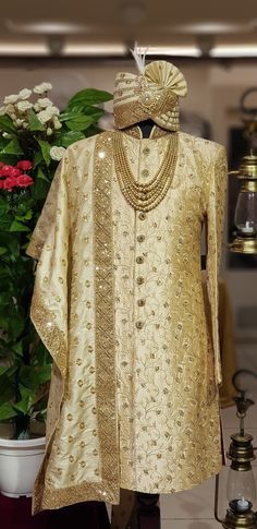 a gold colored outfit is on display next to a potted plant with flowers in the background