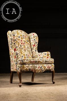 an upholstered chair with floral fabric on the back and arms, in front of a black background