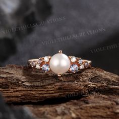 a pearl and diamond ring sitting on top of a piece of wood