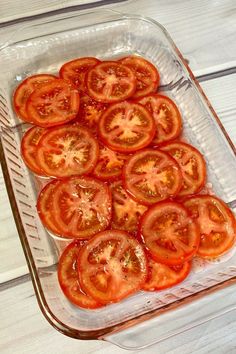 sliced tomatoes in a glass dish on a white wooden table, ready to be cooked