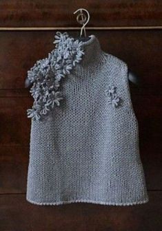 a knitted sweater with flowers hanging on a clothes line next to a wooden door