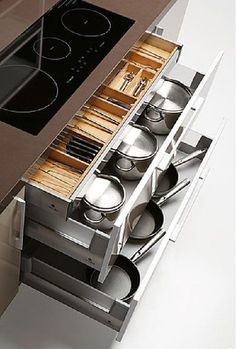 an open drawer with pots and pans in it on the side of a kitchen counter