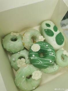 a box filled with green frosted donuts covered in icing and leaf designs