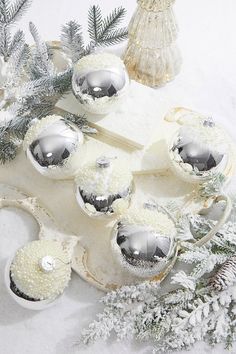 some silver ornaments are sitting on a white surface with snow and pine branches in the background