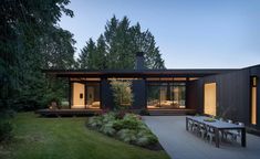 a modern house in the middle of a lush green yard at dusk with patio and dining table