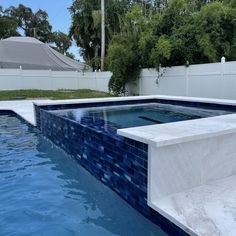 an empty swimming pool with blue tiles on the sides and white fence in the background