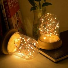 two glass jars with fairy lights in them sitting on a table next to a book