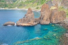 an aerial view of the ocean with rocks and clear blue water in the foreground