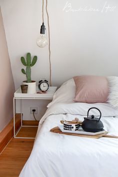 a white bed topped with pillows next to a table and potted cactus on top of it