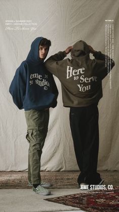 two young men standing next to each other in front of a white wall wearing hoodies