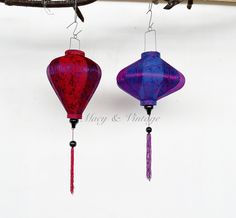 two red and purple lanterns hanging from a tree branch in front of a white wall