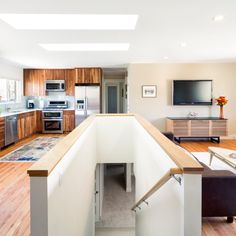 an open kitchen and living room with wood flooring, white walls and wooden cabinets