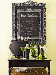 a black table topped with lots of bottles and glasses next to a chalkboard sign