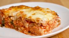 a white plate topped with lasagna covered in cheese and sauce on top of a wooden table