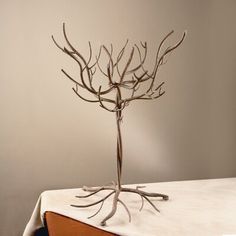 a metal tree sculpture sitting on top of a wooden table next to a white wall