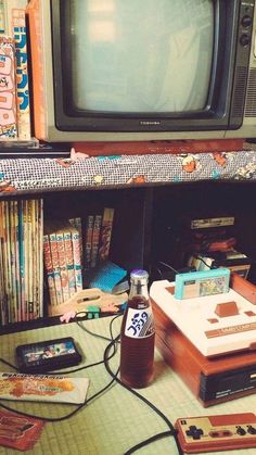 an old tv sitting on top of a table next to a pile of books and video game controllers