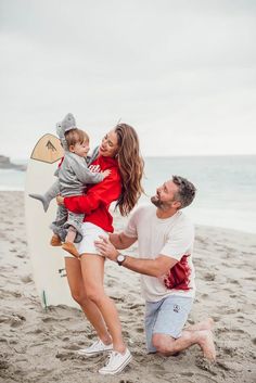 a man kneeling down next to a woman holding a baby on top of a surfboard