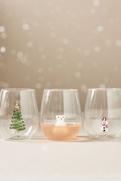 three wine glasses with christmas decorations on the bottom and one has a small tree in it