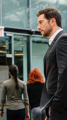 a man standing in front of a glass building with people walking around him and talking to each other