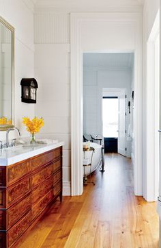 a white bathroom with wood floors and two sinks on the vanity, along with an open door leading to another room